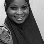 A captivating black and white portrait of a smiling woman wearing a hijab, conveying warmth and cultural beauty.